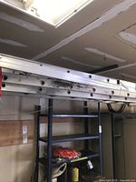 Side view of aluminum ladder resting on garage shelf, showing multiple sections and rungs.