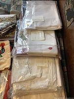 Photo showing stacks of white linens, some wrapped in plastic with handwritten labels.