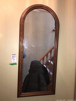 Photo of a rectangular wall-mounted mirror with an arched top in a wood frame reflecting a staircase.