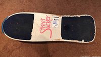 Top view of skateboard deck with Street Sucker logo and worn blue grip pads