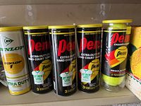 Five sleeves of tennis balls including 4 black Penn Championship Extra-Duty Hard Court Surface sleeves and 1 white Dunlop Extra Duty sleeve.