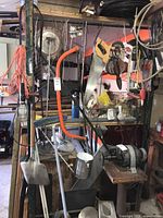 Garage wall displaying various hanging tools including saws, circular saw blade, shovel, extension cords, and hanging caged lamp.