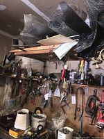 Wide view of garage wall with assorted hanging tools and rolls of wire mesh above shelf