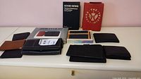 Multiple wallets in black and brown leather and canvas, two religious books, one black and one red cover, and a portfolio folder.