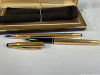 Pen and pencil with rolled gold finish alongside an open presentation box containing felt wraps.