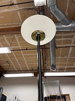 View looking up showing large circular white ribbed glass shade with brass center fitting and black tension rod extending upwards.