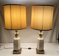 Pair of illuminated Lenox table lamps with cream silk double layer shades and white ceramic bases on metal stands.