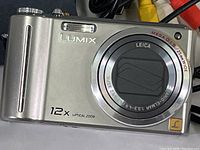 Front view of Panasonic Lumix DMC-ZS1 camera showing lens and zoom markings