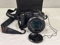 Front view of Sony RX10 camera with lens cap off and canvas pouch visible behind
