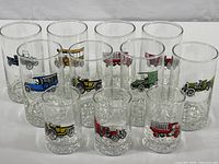 Eleven glasses visible in two sizes, decorated with colorful images of vintage 1910s cars and trucks on clear glasses with hob nob bottoms.