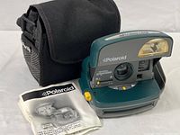 Polaroid OneStep Express camera placed next to instruction manual and carrying case on white background.