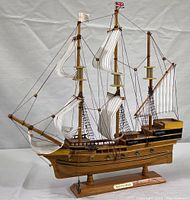Front view of the wooden Mayflower model ship showing all three masts with white fabric sails and rigging, mounted on wooden base.