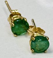 Close-up image showing green round emerald stones in yellow gold prong settings with butterfly backs.