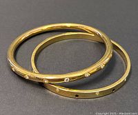 Two gold-tone Swarovski bangles stacked on black background showing clear crystals embedded on the surface.