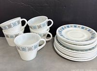Group photo of all five Pyrex trio tea sets (cups, saucers, side plates) stacked on black background. Also shows extra matching plates.
