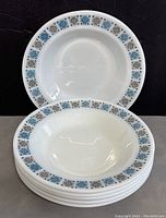 Front view of stacked white ceramic soup plates showing the blue and brown geometric snowflake pattern border.