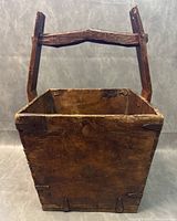 Front view of antique square wooden rice basket with carved handle showing wood grain and joining details.