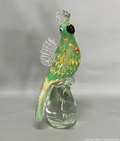 Front side view of the art glass green parrot figurine on clear glass base