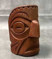 Front side view of the hand carved wooden mask showing the oval eye, rounded nose, geometric carved patterns and sawtooth top edge.