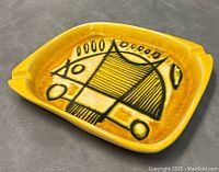 Angled front view of yellow ceramic dish with black modernist abstract design inside, showing color and details.