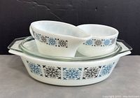 Front view of the set showing sugar bowl with spout, creamer, and casserole dish with lid and blue and black geometric pattern on white glass.
