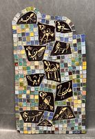 Full front view of rectangular mosaic wall art with colorful small square tiles and inset black tiles with gold designs of birds and animals.