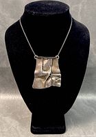 Front view of the textured modernist pendant hanging on a black cord displayed on a black jewelry bust.