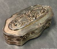Oblique view of the quadruple plated Art Nouveau jewelry casket showing embossed relief of a female face with floral decoration on top and sides, with minor surface tarnish and wear.