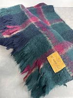 Vintage mohair throw blanket or wrap scarf folded showing fringed edges and plaid color pattern including green, blue, and red hues.