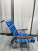 Side angle view of a blue striped Outbound beach chair showing metal frame and wooden armrests.