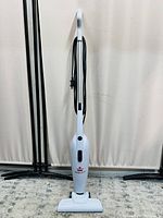 Front view of white Bissell Featherweight stick vacuum cleaner standing upright showing cord wrapped around handle and vacuum head on floor.