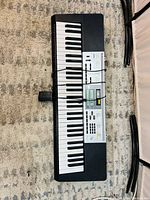 Complete top view of Casio LK-260 keyboard showing keys, control panel, and power adaptor placed on carpet.