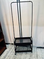 Front view of black metal garment rack with two mesh shelves and hanging bar.