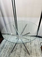 Clear view of round clear glass tabletop with chrome metal legs arranged in a star-like pattern underneath.
