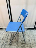 Side angle view of blue foldable chair showing metal frame and blue plastic seat and backrest.