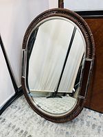 Frontal view of the oval wall mirror showing chocolate-toned rattan frame with stainless steel accents and clear mirror surface.