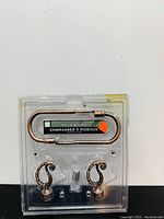 Front view of brand new curtain hold backs in original packaging showing two hold backs with decorative scrolls and connecting rod.