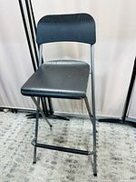 Front angled view of IKEA portable folding chair showing black seat and backrest, metal frame and foldable design on grey carpet