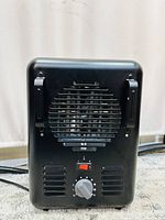 Rear view of black portable space heater showing fan, power switch with two heat settings, and temperature control knob