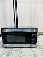 Front view of a stainless steel microwave oven with black windowed door and digital control panel on right side.