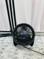 Photo of black Honeywell mini desk fan showing front grille and three blades, standing on carpeted floor with power cord visible.