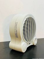 Side angle view of the white portable heater fan, showing rotary controls and warning label on the side.