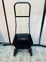 Front view of black Rolser trolley showing two wheels, metal frame handle, and fabric bag with flap cover.