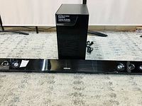 Front view of Samsung soundbar and wireless subwoofer, showing soundbar length and speaker grills, and glossy subwoofer.
