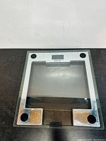 Front view of the scale showing the transparent glass platform with circular black pads and digital display area.