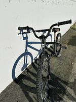 Side view of black stunt bike leaning against a white wall, showing tubeless tire and frame details.