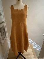 Front view of cinnamon coloured sleeveless linen dress on a mannequin showing square neckline and mid-length design.