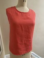 Front view of coral sleeveless linen top on dress form showing neckline and fabric texture.