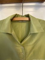 Close-up front view of the blouse collar and upper part, showing the soft green silk fabric and the first mother of pearl button.