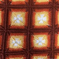 Close-up photo of the granny square crochet pattern showing cream, golden yellow, tangerine, and dark cinnamon colors in the yarn.